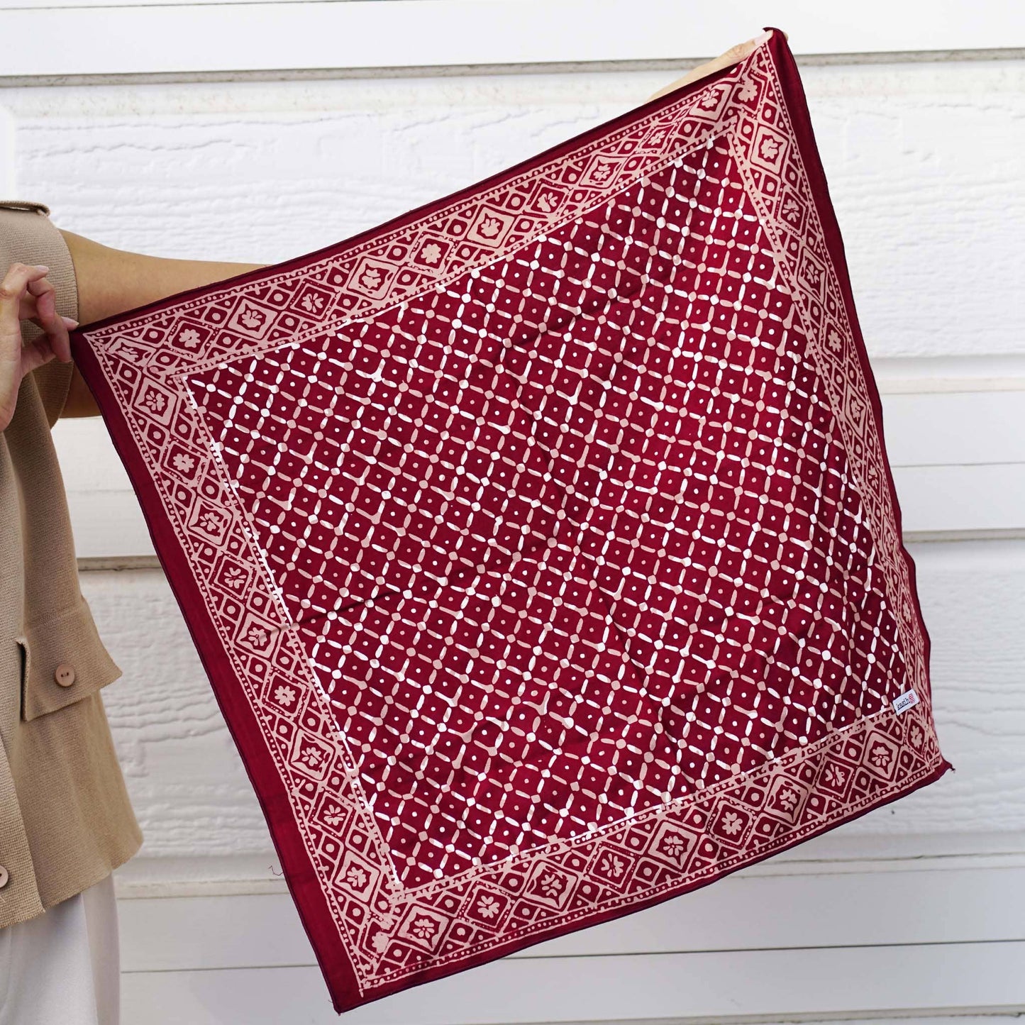 Red patterned fabric held by a person against a white wooden background