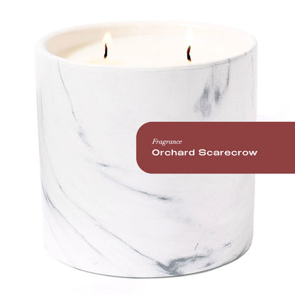 Marble-patterned candle with 'Orchard Scarecrow' fragrance label on a white background