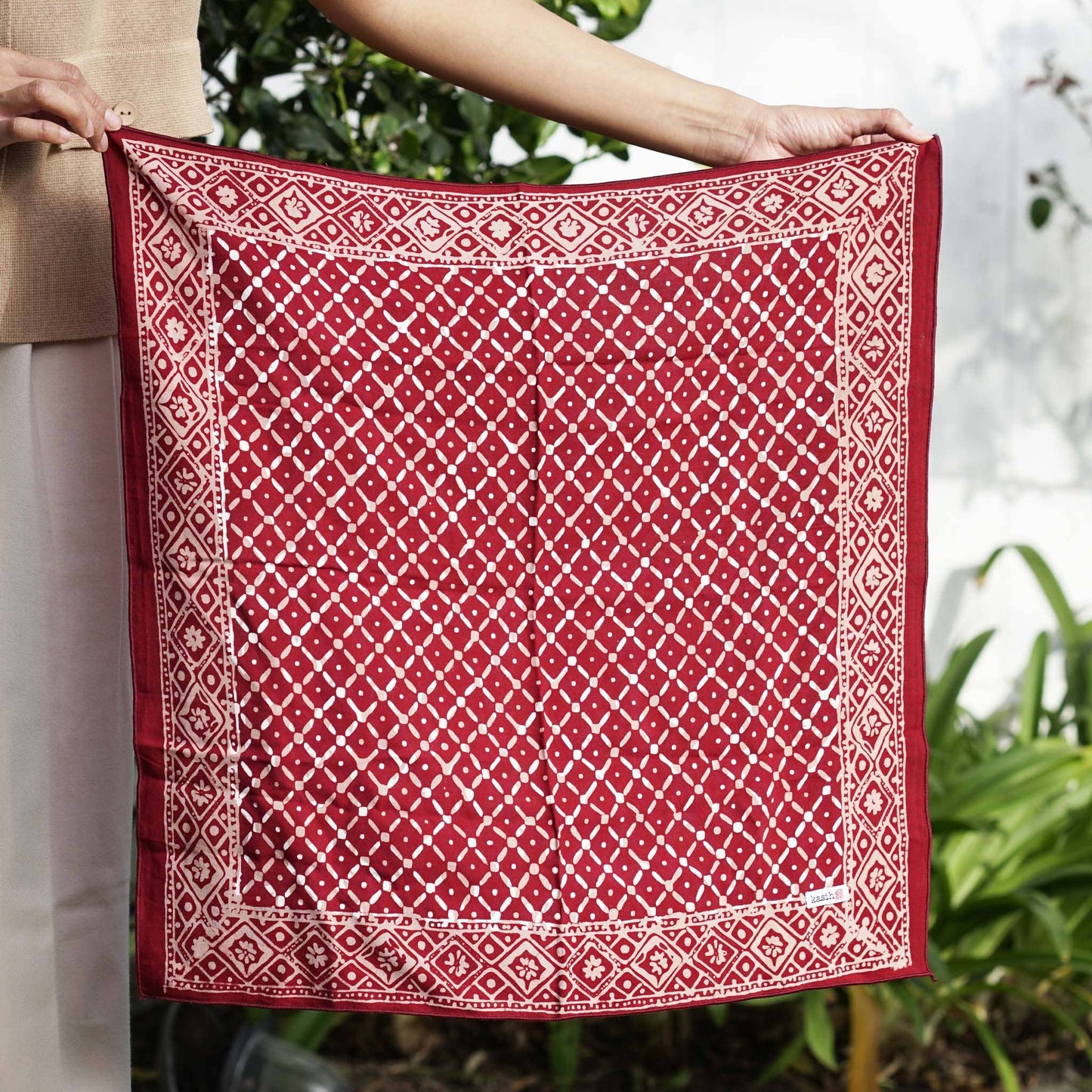 Red and white patterned fabric held by a person with a blurred natural background