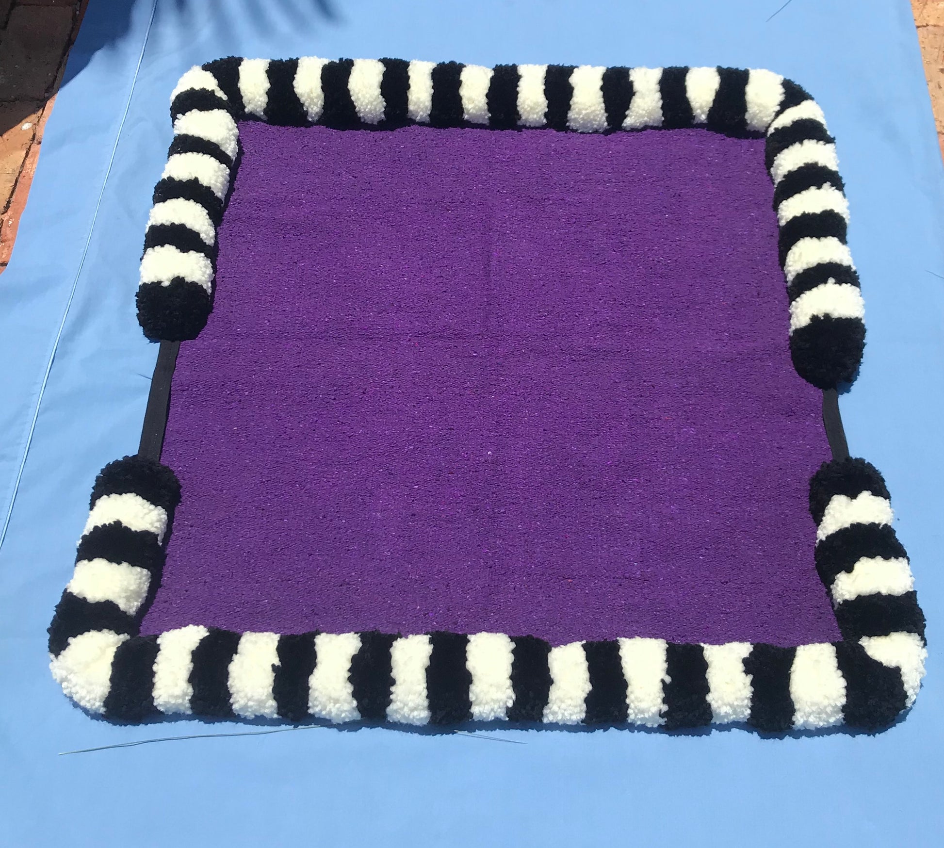 Handmade corona blanket. Black and white pompoms on a purple blanket.