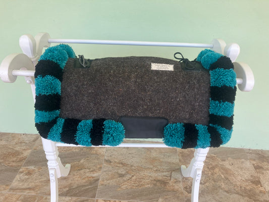 Gray saddle pad with teal and black striped edges draped over a white rack against a light green wall.
