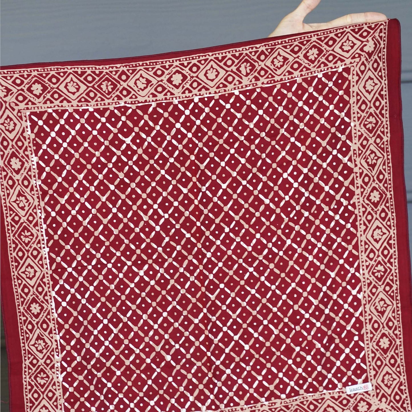 Red fabric with white geometric pattern held by a hand against a gray background