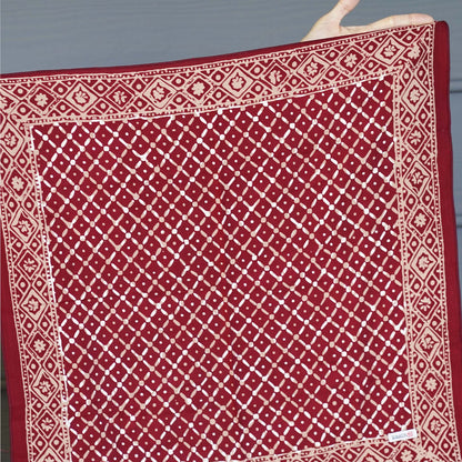 Red fabric with white geometric pattern held by a hand against a gray background