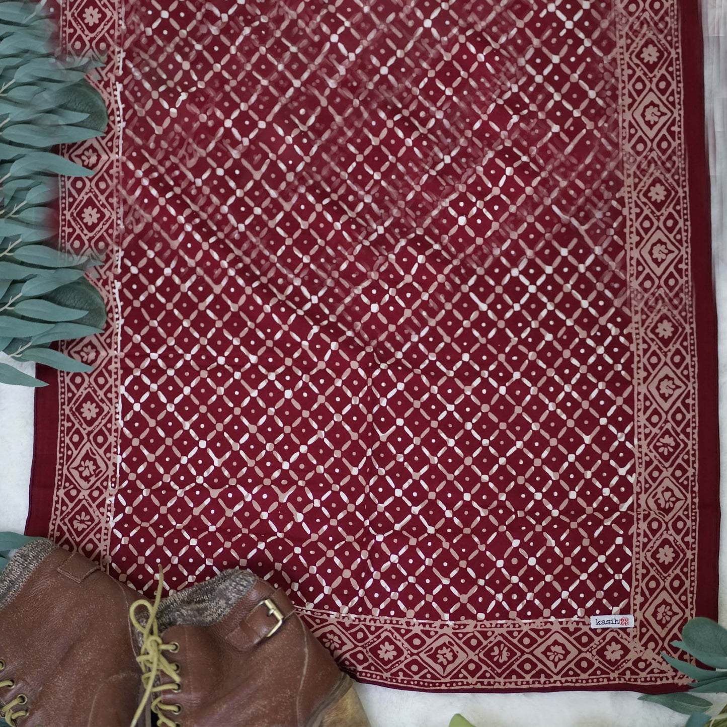 Red patterned fabric with a white geometric design, placed on a surface with green leaves on either side.