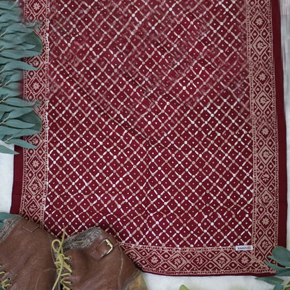 Red patterned fabric with a white geometric design, placed on a surface with green leaves on either side.